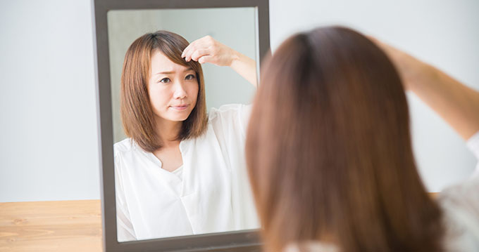 鏡を見て前髪を気にしている女性